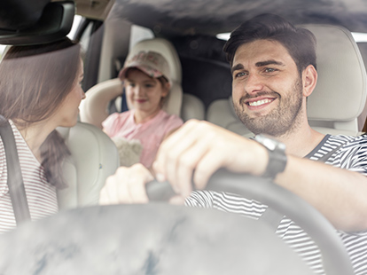 A man driving a car with his wife and daughter.