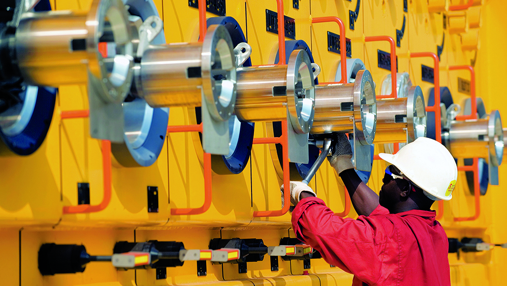 ExxonMobil employee wearing a white hard hat and red uniform inspecting metal onsite